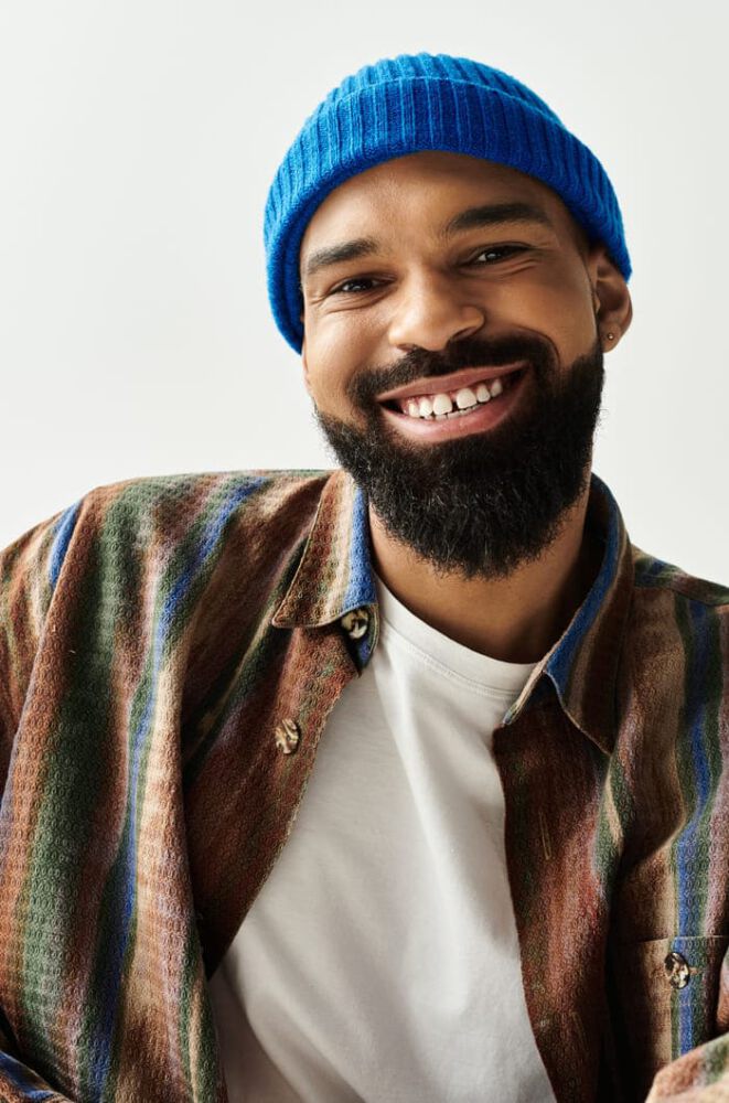 Homme assis de manière décontractée, mettant en valeur son sens de la mode avec un sourire joyeux et une attitude détendue.