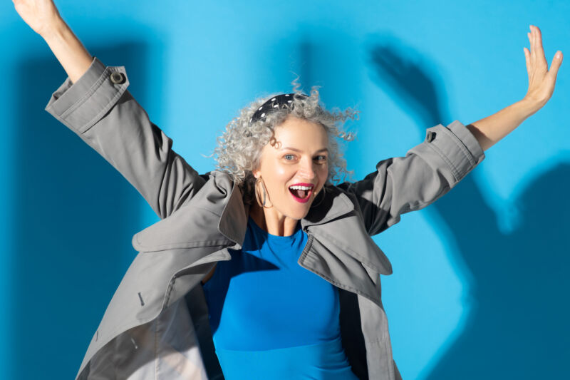 Femme portant une robe bleue et un trench gris, se sentant heureuse et inspirée.