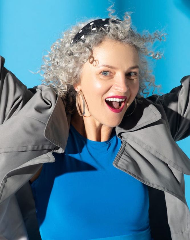 Femme portant une robe bleue et un trench gris, se sentant heureuse et inspirée.