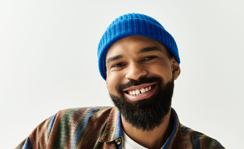 Homme assis de manière décontractée, mettant en valeur son sens de la mode avec un sourire joyeux et une attitude détendue.