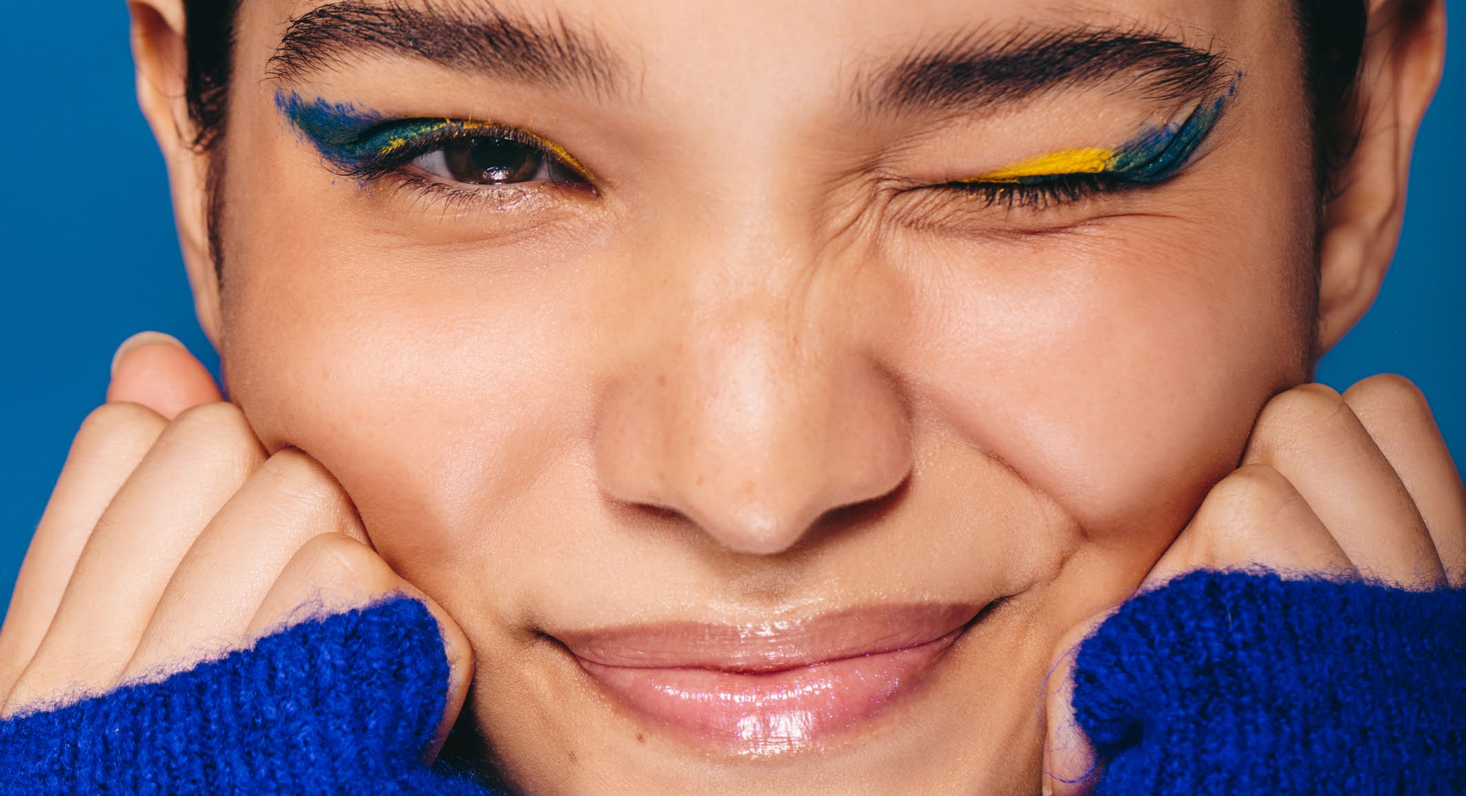 Portrait of a smiling young woman with blue and yellow make-up, winking at the camera